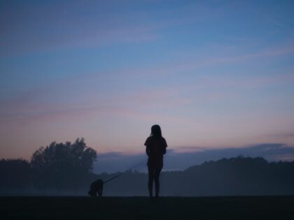 Woman walks dog at dusk.