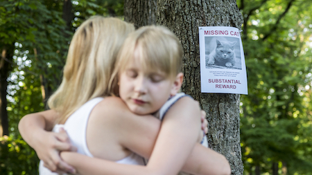 A mother comforts her daughter near a lost cat sign.