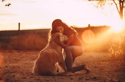 A woman hugs her retriever at sunset.