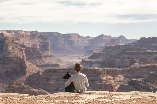 A woman and her dog sit on the edge of a canyon.
